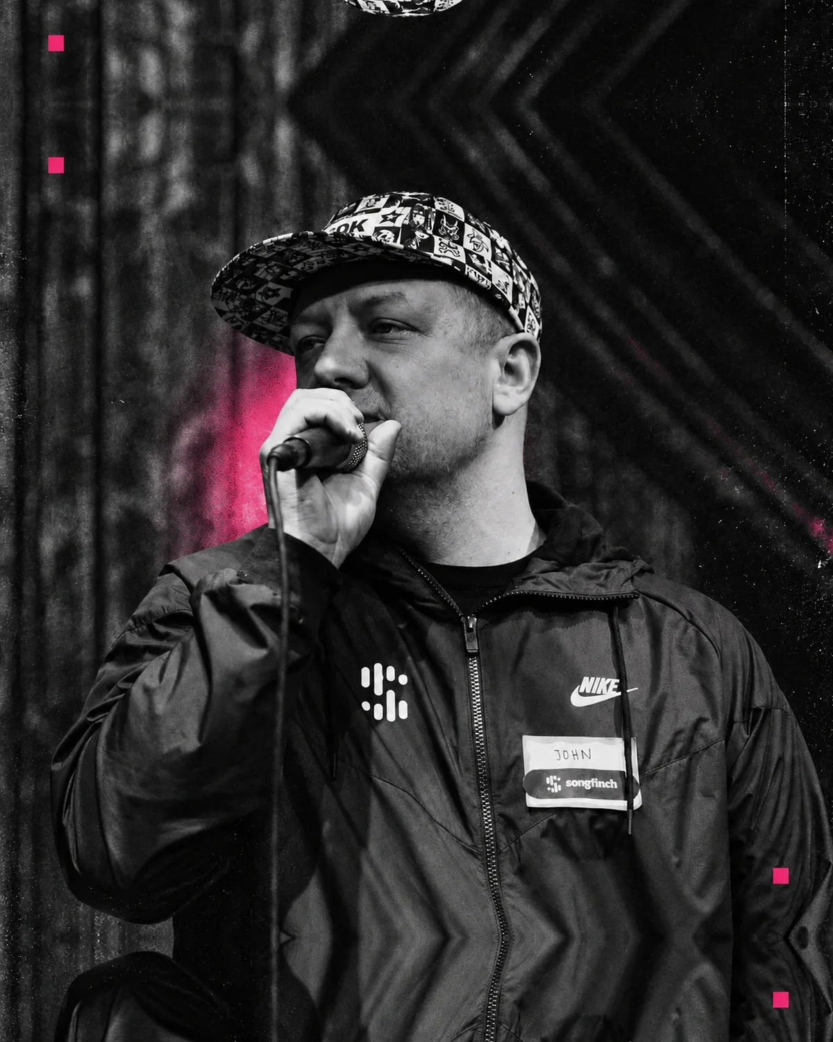 John Williamson on stage with a microphone, in black and white with a pink stage light behind him